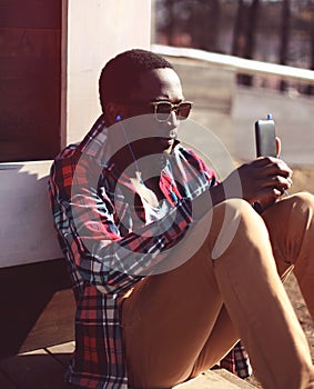 Stylish young african man listens to music and using smartphone,