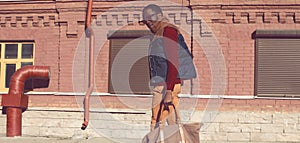 Stylish young african man model posing wearing sweater with bag on city street background