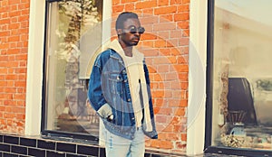 Stylish young african man model wearing denim jacket posing on city street over brick wall background