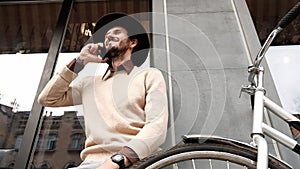 Stylish young bearded man with bicycle answering phone call