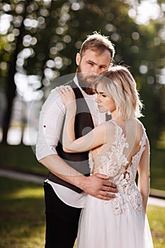 Stylish young beautiful couple hugging in spring park on a sunny day. wedding portrait. Woman in white dress.