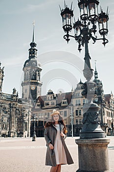 Stylish young beautiful girl in a coat and hat near a lamp in the old city of Dresden.Germany.Walking around the city in Germany