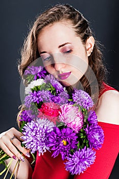 Stylish young beautiful girl who lowered her eyes with purple asters on dark background