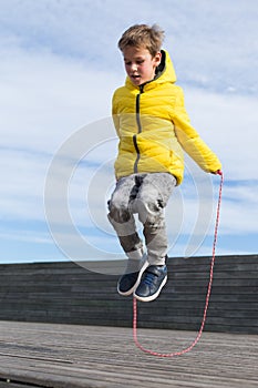 Stylish young boy, teenager is jumping with skipping rope, outdoors