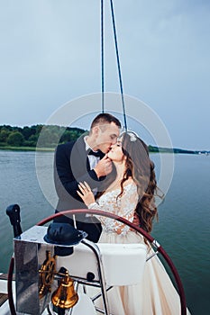 Stylish young bride and groom huging and kissing on board the yacht. Honeymoon sailing