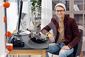 Stylish young brown-haired man sitting at table with typewriters