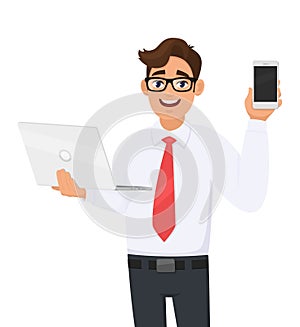 Stylish young business man holding laptop and showing mobile, cell phone. Trendy person using or working computer. Male character.