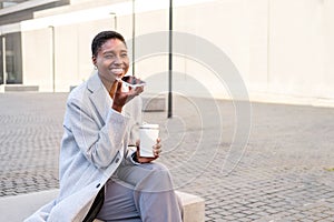 Stylish young business woman sitting and taking a break outdoors while sending voice message with phone