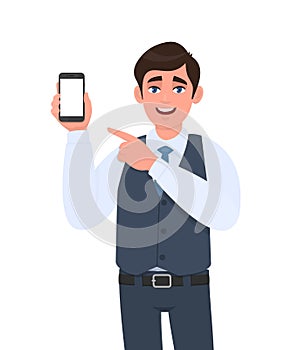 Stylish young businessman in vest suit showing blank mobile, cell phone and pointing finger. Trendy person holding smartphone.