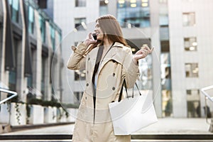 Stylish young businesswoman walks down the stairs in the middle of the street carrying shopping bag, talks on phone , style and