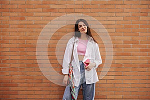Stylish young caucasian woman in stylish casual clothes posing near brick wall on street.