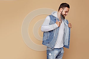 Stylish young cheerful guy with a beautiful beard in a denim jacket and white t-shirt on a plain cream background. Denim
