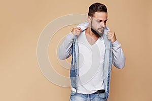 Stylish young cheerful guy with a beautiful beard in a denim jacket and white t-shirt on a plain cream background. Denim jacket