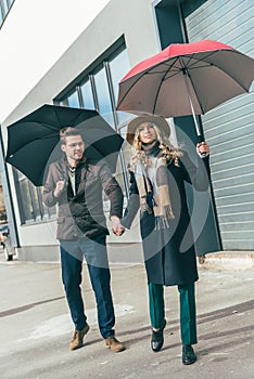 stylish young couple in autumn outfit holding umbrellas