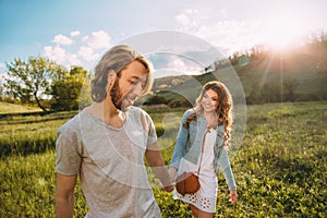 Stylish young couple. Film photo at sunset and with a sunlight. A guy with a stylish haircut pulls by the hand and a red