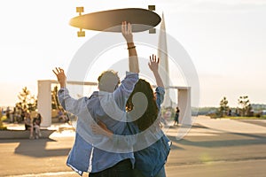 Stylish young couple hug looking at sunset hold skateboard. Happy girl and guy in love enjoy freedom