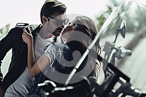 Stylish young couple hugging and kissing on motorcycle outdoors