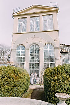 Stylish young couple near the old beige house with columns and big vintage windows. Romantic wedding in Paris