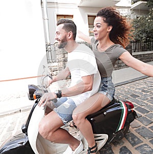 Stylish young couple sits a scooter in the street.