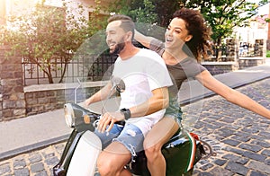 Stylish young couple sits a scooter in the street.