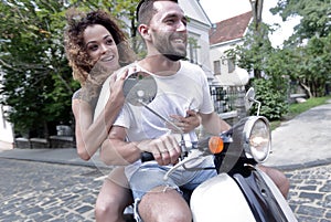 Stylish young couple sits a scooter in the street.