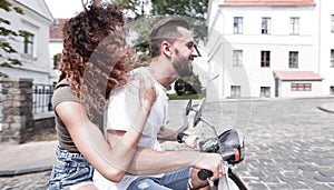 Stylish young couple sits a scooter in the street.