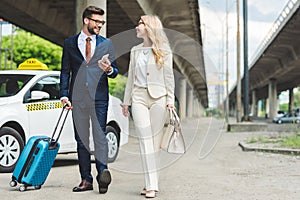 stylish young couple smiling each other while going with suitcase
