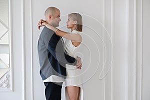 a stylish young couple stands, hugging and looking at each other with loving eyes