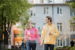 Stylish young couple in sunglasses with coffee cups holding hands and walking