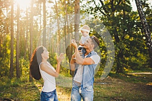 Stylish young Family mom, dad and daughter one year old blonde sitting with father on shoulders playing happy and smiling, outdoor