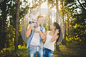 Stylish young Family of mom, dad and daughter one year old blonde sitting near father on shoulders, outdoors outside the city in a