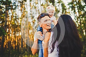 Stylish young Family of mom, dad and daughter one year old blonde sitting near father on shoulders, outdoors outside the city in a