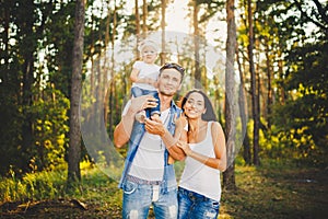 Stylish young Family of mom, dad and daughter one year old blonde sitting near father on shoulders, outdoors outside the city in a