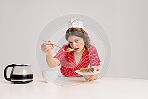 Stylish young female waitress in retro american fashion style of 70s, 80s sitting at table and drinking coffee over grey