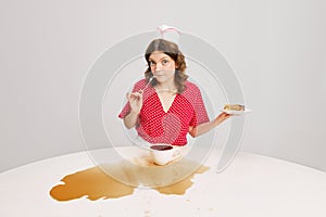 Stylish young female waitress in retro american fashion style of 70s, 80s sitting at table and drinking coffee over grey