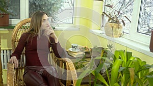 Stylish young girl with beautiful make-up sitting in a wicker rocking chair and looking out the window