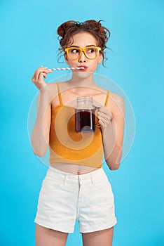 Stylish young girl is drinking soda water on blue background