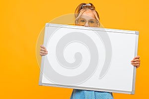 Stylish young girl holding a white board with a mockup on a yellow background