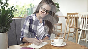 Stylish young girl writes in the journal in cafe
