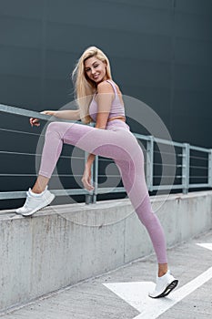 Stylish young happy woman with slim fitness body in fashion sportswear with white running shoes posing in the city