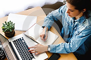 stylish young hipster girl working economist financial analytics holding pen on craft background with laptop and