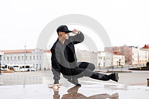 Stylish young male dancer in fashionable black clothes dancing blake dance on a street in the city on an autumn afternoon