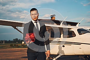 Stylish young man with gift box standing at airdrome