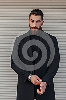 Stylish young man with a hairdo and beard in a trendy black coat