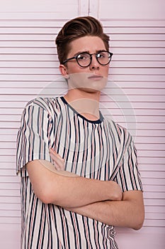 Stylish young man hipster in fashionable glasses with a hairstyle in a trendy striped t-shirt posing near a vintage wooden pink