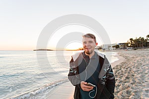 Stylish young man listen to music in headphones on a smartphone at the beach. Lifestyle, technology and people concept