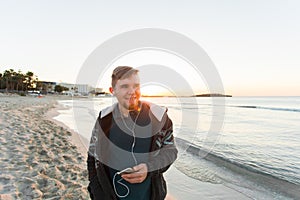 Stylish young man listen to music in headphones on a smartphone at the beach. Lifestyle, technology and people concept