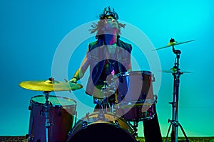 Stylish young man, musician playing drums, making solo performance against blue background in neon light