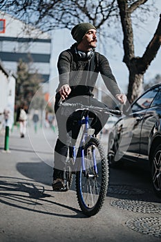 Stylish young man riding a bicycle with headphones in the city