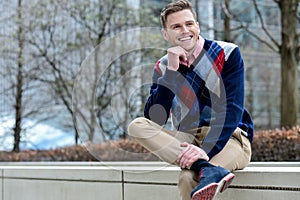 Stylish young man sitting in sidewalk